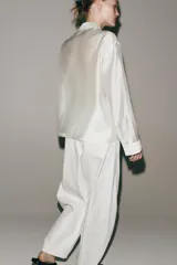 Camisa de estilo oriental confeccionada en mezcla de lyocell con acabado satinado. Presenta cuello redondo, manga larga con puños rectos, bolsillos de plastrón y cierre frontal mediante alamares.