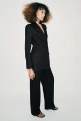 Blazer de cuello solapa y manga larga con hombreras marcadas. Presenta un diseño cruzado con cierre frontal de botones a presión, bolsillos delanteros con solapa y un detalle de cintura entallada con efecto abullonado.