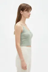 Musculosa de punto blanco, corte crop, con tirantes finos, escote en V adornado con detalles de encaje y un pequeño lazo en el centro.