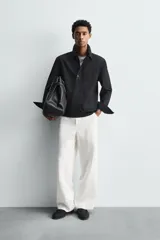 Camisa polo de denim negro con mezcla de algodón y cáñamo. Cuello polo con cierre frontal de tres botones. Manga larga con puño abotonado. Bolsillos de plastrón en el pecho y en la cadera.