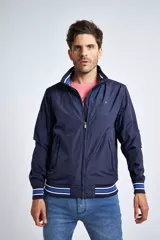 Campera liviana de nylon color gris oscuro, con cierre frontal completo, cuello subido y puños y cintura acanalados con rayas en rojo y blanco. Presenta logo bordado en el pecho y bolsillos laterales con cierre.