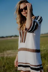 Vestido corto tejido en hilo de algodón color blanco con rayas horizontales marrones y negras, escote en V y mangas cortas.