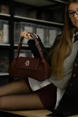 Cartera tipo baguette de cuero nobuk color musgo con detalles en cuero marrón. Tiene correa al hombro regulable, cierre YKK de aluminio plateado, chapa de marca central y logo grabado en la parte trasera.