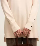 Suéter de punto color crema, con cuello alto, mangas largas y botones decorativos en los puños.