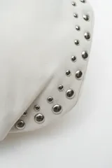 Cartera tipo hobo bag color negro, con detalles de tachas plateadas en los bordes y un charm colgante en forma de corazón también con tachas.