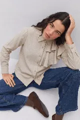 Camisa de lino color beige, con cuello clásico, cierre frontal de botones y detalle de volado lateral en el frente. Posee mangas largas con puños abotonados.