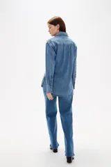 Camisa de jean negro con diseño de frunces verticales en el frente, cuello clásico, cierre frontal con botones y mangas largas con puños abotonados.