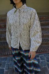 Sobrecamisa de pana con estampado floral pequeño en tonos marrones sobre base cruda. Presenta cuello clásico, cierre frontal con broches metálicos y mangas largas abullonadas.