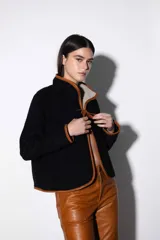 Chaqueta corta negra de paño con ribete de cuero color marrón en todo el contorno. Se ata con una tira de cuero en el centro y tiene dos bolsillos laterales.