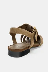 Sandalia plana tipo cangrejera en serraje color marrón claro, con tiras entrelazadas en la parte delantera y cierre de hebilla en el tobillo. Tiene punta redonda y un tacón bajo de 2 cm.