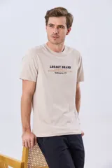 Remera de algodón color beige con cuello redondo y mangas cortas. Presenta un estampado frontal con letras en tonos azul y marrón con la inscripción "Legacy Brand Southampton, NY".