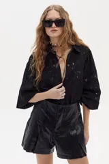 Camisa negra de encaje de algodón con cuello camisero clásico, mangas largas abullonadas con puños elásticos y cierre frontal con botones de nácar.