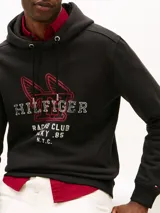 Buzo con capucha Tommy Hilfiger de color negro, con cordones ajustables y un diseño gráfico bordado en el pecho que incluye inscripciones de estilo universitario y automovilístico.