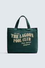 Bolso tipo shopper de algodón en color verde oscuro, con diseño de estampado tipográfico en color crema en el frente. Cuenta con dos asas de mano y cierre magnético.