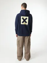 Hoodie azul marino con capucha, bolsillo tipo canguro y gran estampado cuadrado en la espalda con una letra X negra sobre fondo beige.