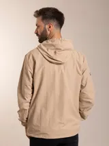 Campera de nylon con capucha, cierre frontal y forro de red. Presenta un diseño minimalista en color beige con detalles en negro.