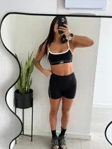 Conjunto deportivo de dos piezas en color negro, compuesto por un top deportivo con tirantes y ribetes blancos, y un short ajustado con detalles de líneas blancas en los laterales.