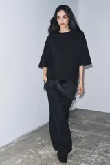 Camiseta de algodón de corte regular, color marrón oscuro o negro, con cuello redondo y manga corta. Presenta un bajo asimétrico con aplicación de encaje negro a tono.