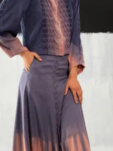 Chaqueta entallada de algodón tipo seda, teñida a mano con técnica tie-dye en tonos azul y naranja. Tiene cuello mao, mangas largas con puños abullonados y cierre frontal con broches.