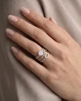 Anillo triple ajustable de acero quirúrgico plateado con detalles de circonias, compuesto por tres bandas: una con un dije circular pavé, otra con aros ovalados y otra con textura de esferas.