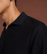 Polo de manga larga color beige claro, confeccionado en tejido texturizado (posiblemente acanalado o waffle). Presenta un cuello polo con escote profundo en V sin botones.