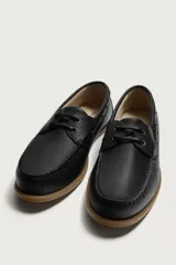 Zapato náutico de piel color beige, con cordones y ojalillos metálicos, suela plana de goma marrón y costuras visibles en la puntera.