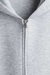 Campera con capucha y cierre frontal, color gris melange, de tejido efecto neopreno. Presenta un corte holgado (boxy) con hombros caídos y bolsillos delanteros abiertos.