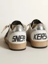 Championes Golden Goose modelo Ball Star, de caña baja, confeccionados en cuero color blanco con detalles en gris y negro. Presentan una estrella negra en el lateral, talón plateado con logo y suela de goma con efecto envejecido.
