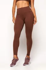 Calza deportiva de tiro alto color marrón, confeccionada en tejido técnico de alto rendimiento con compresión. Presenta bolsillos laterales funcionales y detalles reflectivos para mayor visibilidad.