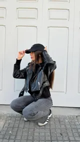 Campera biker de cuero sintético negro con cierre asimétrico, solapas anchas, bolsillos con cierre y cinturón ajustable en la cintura con hebilla metálica.