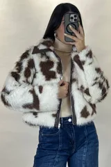 Campera corta de piel sintética con estampado de manchas tipo vaca en tonos blanco y marrón. Presenta cuello camisero, cierre frontal con cremallera y detalles en cuero sintético marrón en el cuello y la solapa del cierre.
