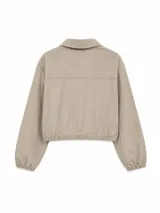 Campera corta de tela técnica con acabado ligeramente arrugado, color beige. Presenta cuello camisero, cierre frontal con botones a presión, mangas largas con puños elásticos y ruedo ajustable con cordón.
