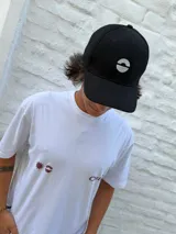 Gorro tipo jockey negro con visera curva y logo frontal bordado en blanco, que representa un semicírculo dividido horizontalmente.