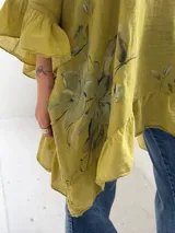 Blusa color verde pistacho, de corte holgado, manga corta con volados y diseño asimétrico con volado en el ruedo. Cuenta con un estampado floral difuminado en el frente.