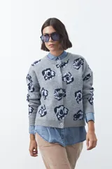 Cardigan de tejido jacquard color marrón con estampado floral en tonos rojo y rosado. Presenta cuello redondo, cierre frontal con botones y terminaciones acanaladas en puños y ruedo.