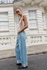Jeans baggy de tiro medio con pernera holgada, diseño de cinco bolsillos y bajo acabado en vuelta. Cuenta con cintura elástica en la espalda y cierre frontal con cremallera y botón.