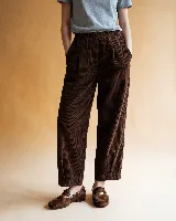 Pantalón de pana color marrón, de corte holgado y largo al tobillo. Presenta cintura elástica, bolsillos delanteros y detalle constructivo en forma de corazón en el bolsillo trasero.