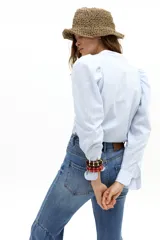 Camisa de popelina de algodón con estampado de rayas verticales celestes y blancas. Presenta cuello mao, cierre frontal con botones de nácar, mangas largas con hombros ligeramente fruncidos y abullonados, y detalles de corazones bordados y aplicados en el frente.