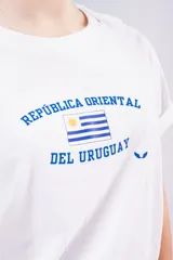 Remera blanca de algodón con cuello redondo y mangas cortas. Presenta un estampado frontal en color azul con la inscripción 'República Oriental del Uruguay' y la bandera nacional.