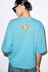 Camiseta oversize de algodón con efecto lavado, color celeste, cuello redondo, manga corta y estampa frontal de la artista Philippa Coules.