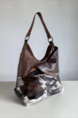 Cartera de cuero combinada con texturas y pelo natural con estampado animal print tipo vaca, diseño envolvente con líneas orgánicas, asa de hombro y bolsillos exteriores.