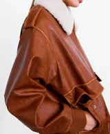 Chaqueta estilo aviador de cuero sintético marrón, con cuello de corderito sintético blanco, bolsillos frontales con solapa, cierre de cremallera y puños y cintura de canalé elástico.