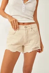 Short de denim color beige, de tiro medio y silueta relajada, con cinco bolsillos, cierre frontal con botón y cremallera, y detalles de roturas y bordes deshilachados.