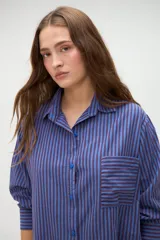 Camisa de manga larga de algodón, con diseño a rayas en tonos azules y morados, calce holgado, cuello camisero, cierre frontal con botones y un bolsillo aplicado en el pecho.