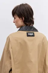 Cazadora de corte oversize en color beige, con cuello de solapa en contraste de color oscuro, cierre frontal con botones y bolsillos laterales.