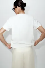 Camiseta blanca de algodón con cuello redondo y manga corta, destacada por aplicación de flores tridimensionales a tono en el frente.