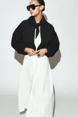 Chaqueta bomber negra con cuello redondo y pañuelo desmontable anudado al frente. Presenta cierre frontal con cremallera, bolsillos laterales con solapa y botones a presión, y terminaciones elásticas abullonadas en puños y ruedo.
