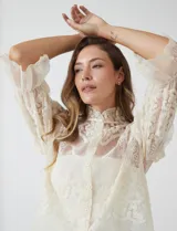 Blusa de tul bordado color beige, marca Liv Los Angeles, con cuello alto, cierre frontal de botones y mangas ¾ amplias con volados.