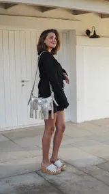 Mini bandolera de cuero con diseño de flecos largos y hebilla frontal decorativa. Presenta un acabado texturizado con efecto craquelado en tonos blanco y marrón, y correa ajustable.