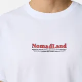 Remera blanca de manga corta, confeccionada en algodón orgánico, con diseño holgado y estampado frontal pequeño con la inscripción "NomadLand" en color rojo y negro.